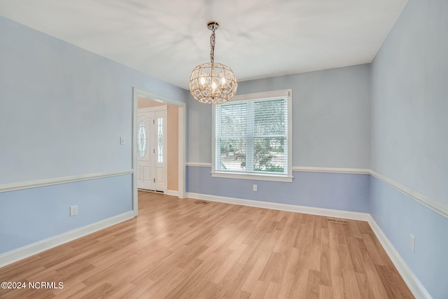 empty room featuring light wood-type flooring and a chandelier