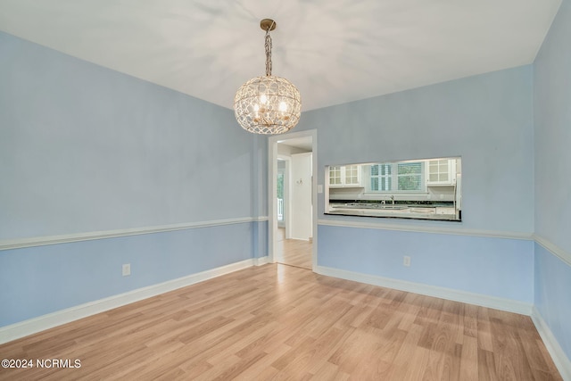 spare room featuring a notable chandelier and light wood-type flooring