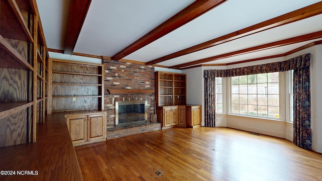 unfurnished living room with brick wall, a brick fireplace, beam ceiling, and dark wood-type flooring