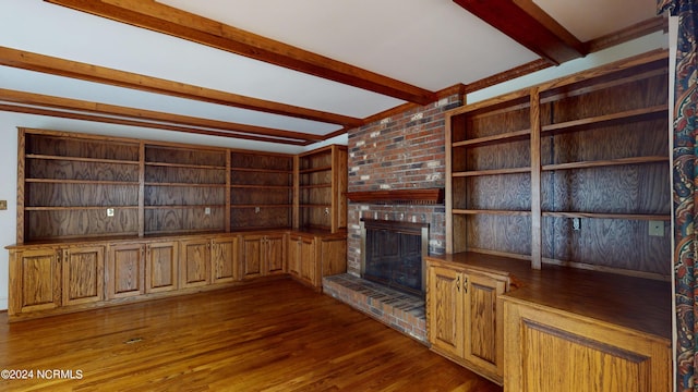 unfurnished living room with brick wall, beamed ceiling, a brick fireplace, and dark hardwood / wood-style flooring