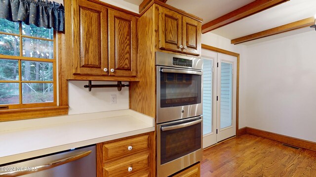 kitchen with built in desk, beamed ceiling, light wood-type flooring, and stainless steel appliances