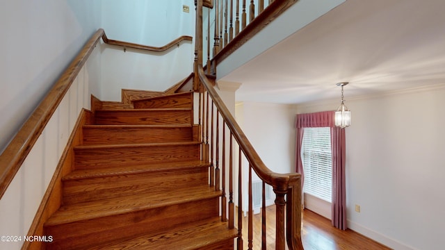 stairway with light hardwood / wood-style floors, ornamental molding, and a chandelier