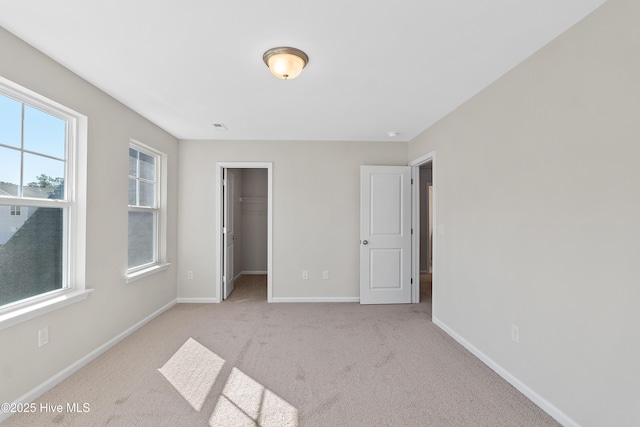 unfurnished bedroom featuring light colored carpet, a spacious closet, and a closet