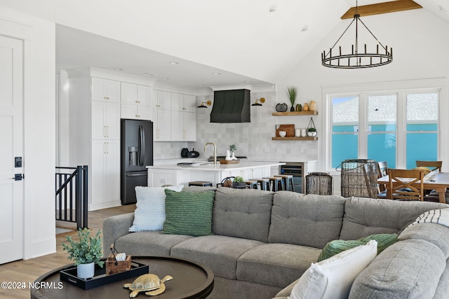 living room featuring a notable chandelier, a water view, light hardwood / wood-style flooring, high vaulted ceiling, and sink