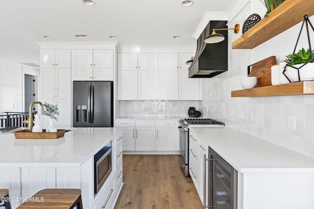 kitchen with appliances with stainless steel finishes, light hardwood / wood-style flooring, wine cooler, white cabinets, and tasteful backsplash