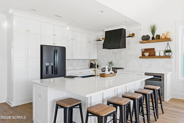 kitchen featuring white cabinets, a breakfast bar, black fridge, and premium range hood