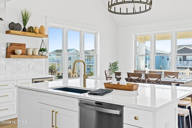 kitchen with a center island with sink, stainless steel dishwasher, white cabinetry, lofted ceiling, and sink