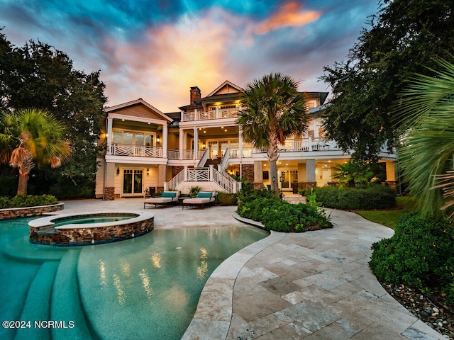 pool at dusk featuring a patio area and an in ground hot tub