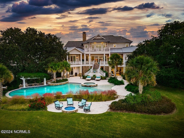 pool at dusk featuring a patio, a yard, an outdoor fire pit, and an in ground hot tub