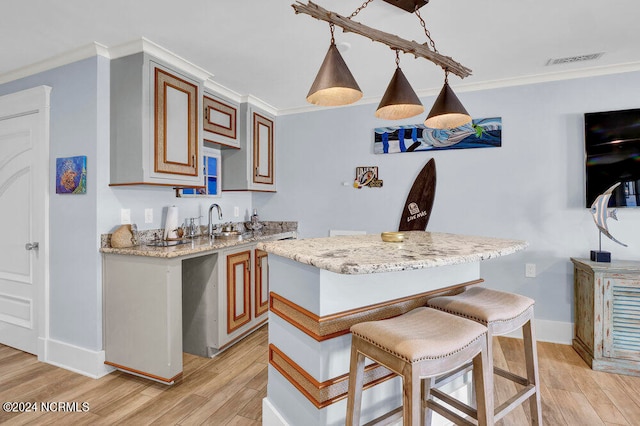 kitchen featuring hanging light fixtures, light wood-type flooring, light stone counters, a breakfast bar area, and crown molding