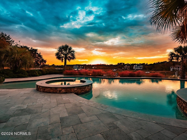 pool at dusk featuring an in ground hot tub