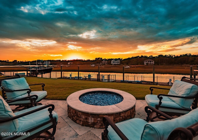 patio terrace at dusk featuring an outdoor fire pit, a water view, and a lawn