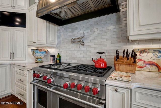 kitchen featuring range with two ovens, backsplash, custom range hood, and light stone countertops