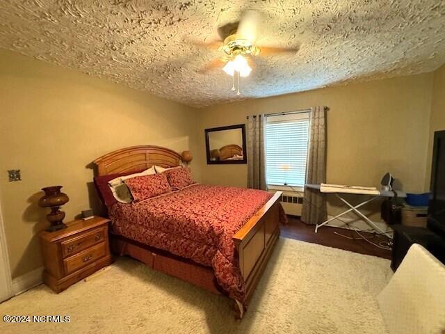 carpeted bedroom featuring a textured ceiling, ceiling fan, and radiator heating unit