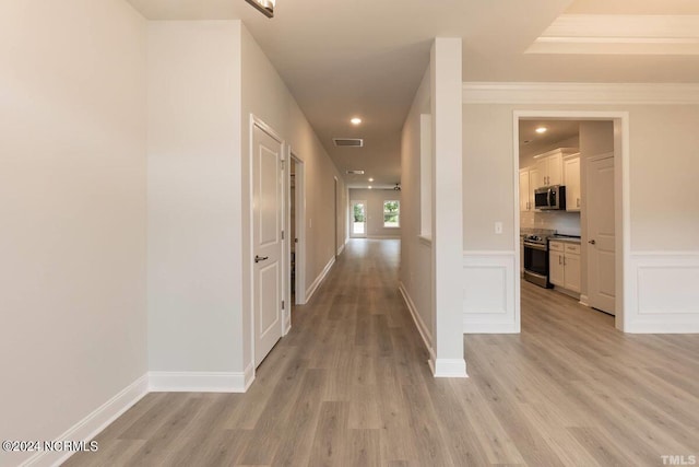 hall with light wood-type flooring, a wainscoted wall, visible vents, and a decorative wall