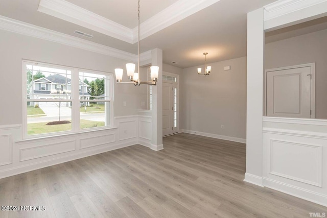 unfurnished dining area with light wood-style flooring, a decorative wall, a notable chandelier, a raised ceiling, and crown molding