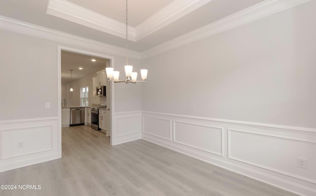 unfurnished dining area featuring light wood finished floors, wainscoting, a tray ceiling, crown molding, and a chandelier