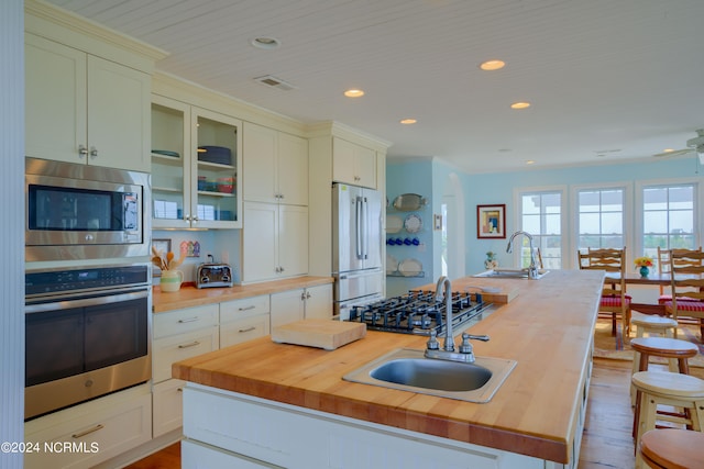 kitchen featuring a kitchen island with sink, stainless steel appliances, sink, and butcher block counters