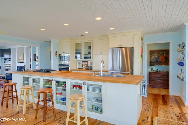 kitchen with a kitchen breakfast bar, stainless steel appliances, light hardwood / wood-style flooring, a center island with sink, and wood counters