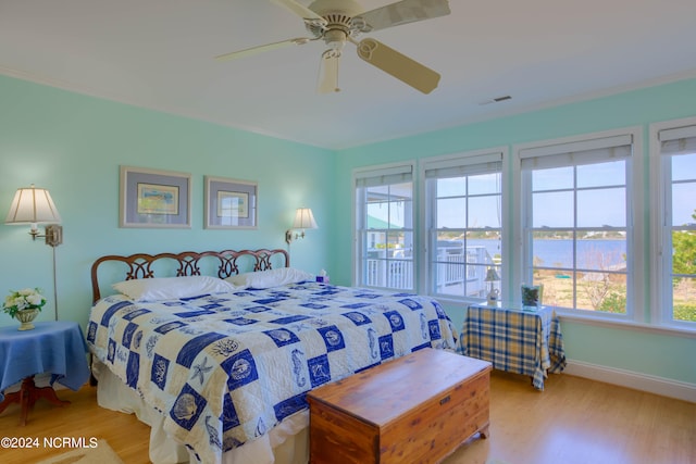 bedroom featuring light wood-type flooring, a water view, and ceiling fan