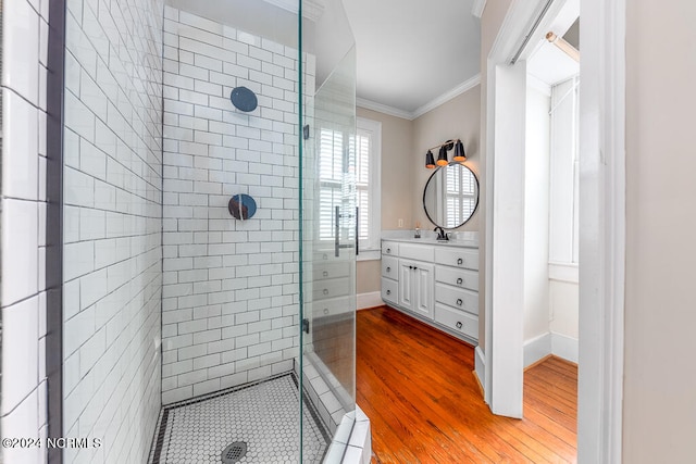 bathroom with wood-type flooring, vanity, ornamental molding, and tiled shower