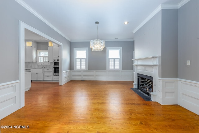 unfurnished living room featuring ornamental molding, an inviting chandelier, and light hardwood / wood-style flooring