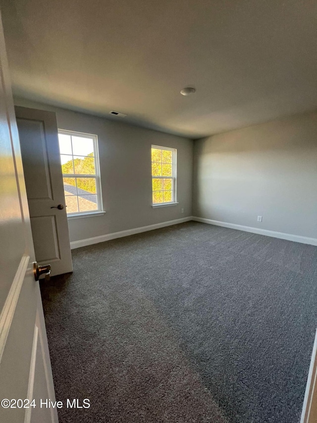 unfurnished room with a healthy amount of sunlight and dark carpet