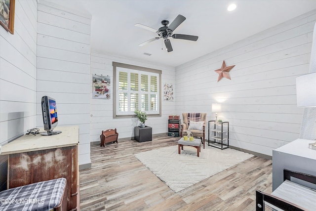 living area featuring light hardwood / wood-style flooring, ceiling fan, and wood walls