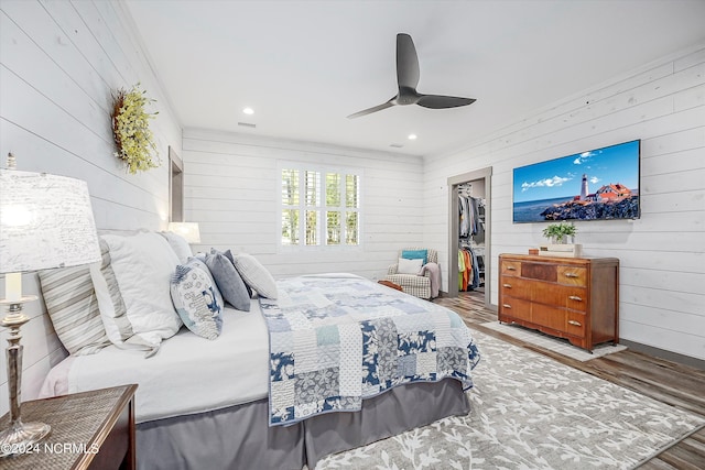 bedroom with a spacious closet, dark hardwood / wood-style floors, a closet, wooden walls, and ceiling fan