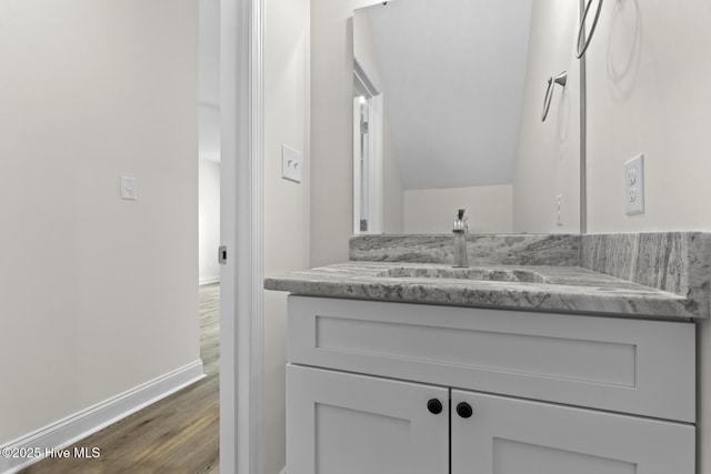 bathroom with vanity, vaulted ceiling, wood finished floors, and baseboards