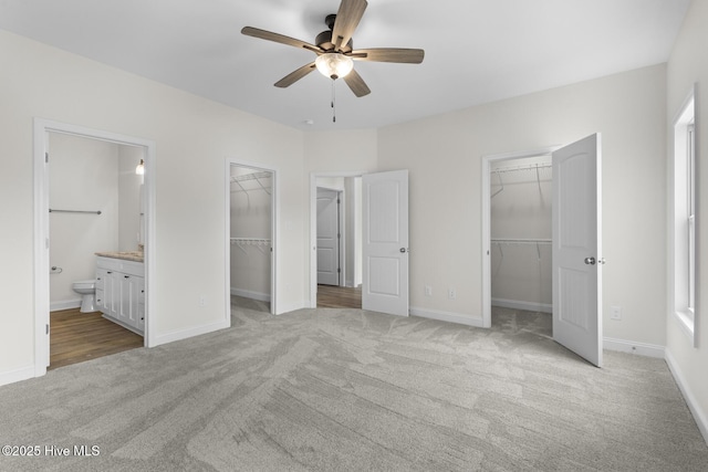 unfurnished bedroom with a walk in closet, a closet, connected bathroom, baseboards, and light colored carpet