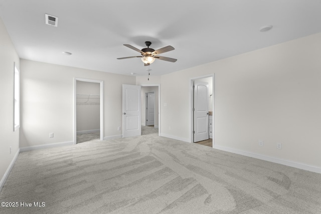 unfurnished bedroom with light colored carpet, a walk in closet, baseboards, and visible vents