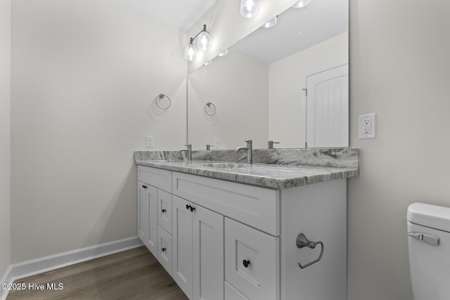 bathroom featuring toilet, a sink, wood finished floors, double vanity, and baseboards