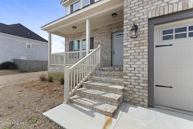 entrance to property featuring brick siding, a porch, and a garage