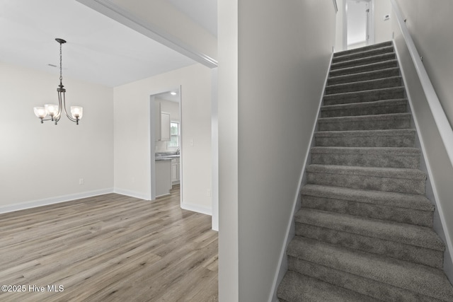 stairs featuring an inviting chandelier, wood finished floors, and baseboards