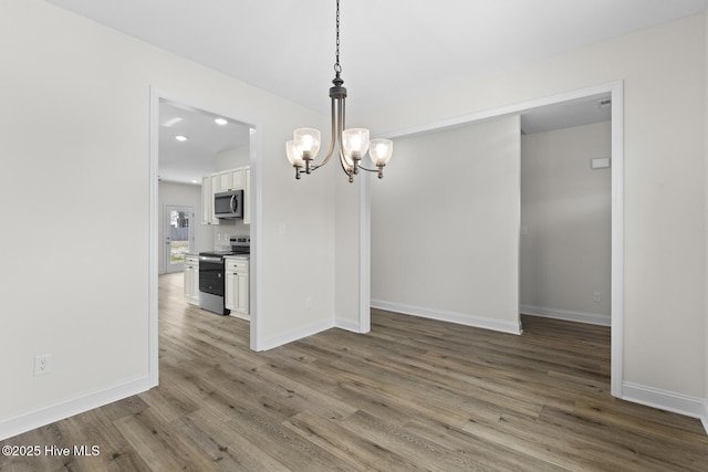 unfurnished dining area featuring baseboards, an inviting chandelier, and wood finished floors