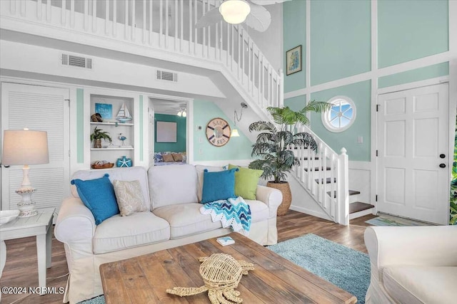 living room featuring hardwood / wood-style flooring, ceiling fan, built in features, and a high ceiling