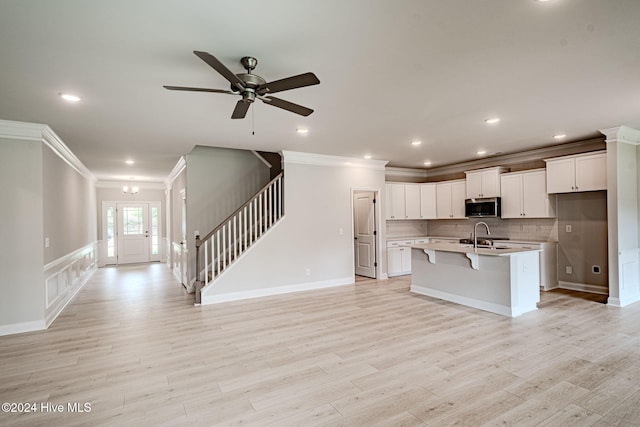 kitchen featuring white cabinets, light wood-type flooring, an island with sink, ornamental molding, and a kitchen bar