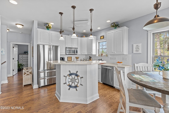 kitchen featuring dark hardwood / wood-style floors, pendant lighting, white cabinets, appliances with stainless steel finishes, and a center island