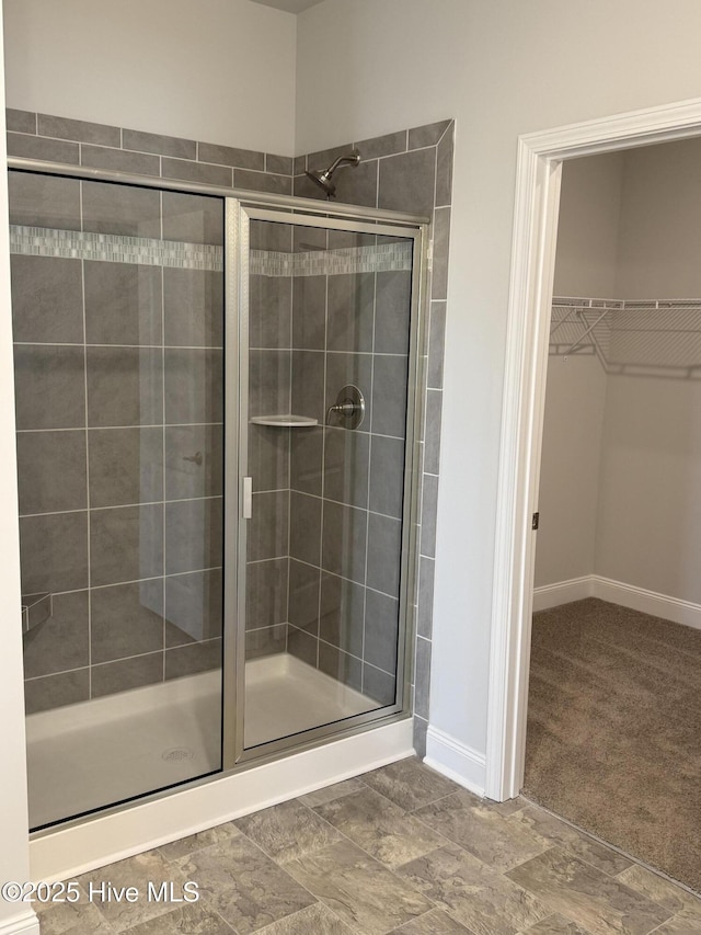 full bath featuring baseboards, a spacious closet, and a shower stall