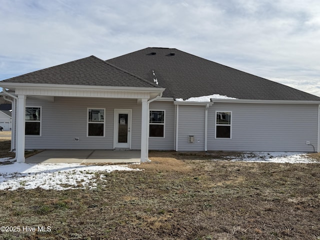 snow covered rear of property with a patio and a shingled roof