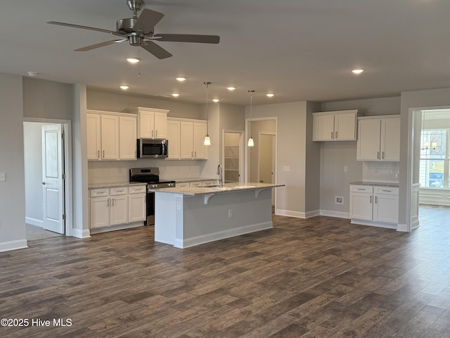 kitchen featuring an island with sink, appliances with stainless steel finishes, light stone counters, dark wood-style flooring, and white cabinetry