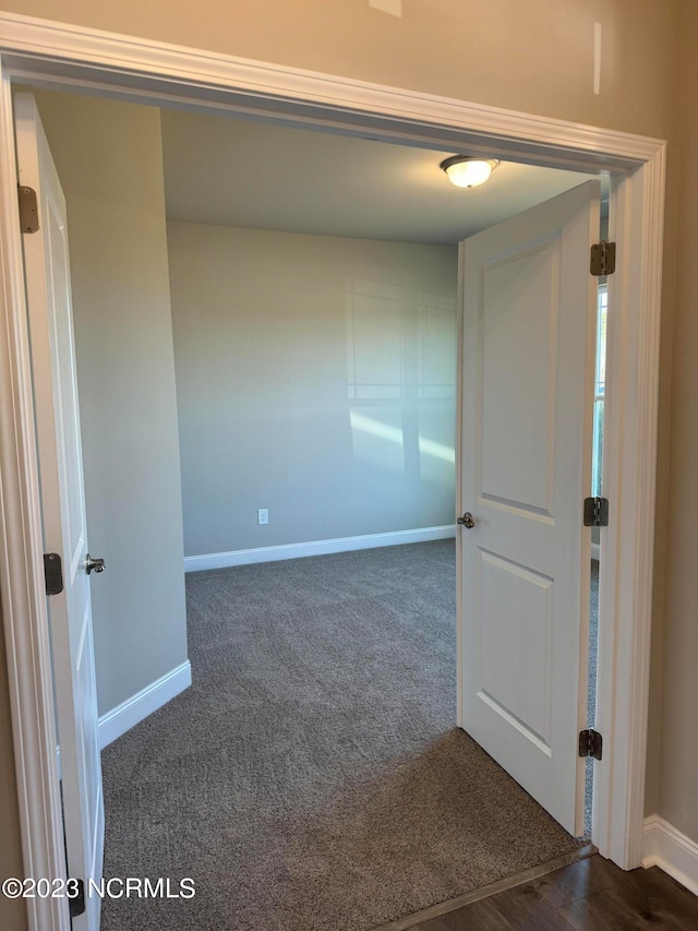 unfurnished room featuring dark colored carpet and baseboards