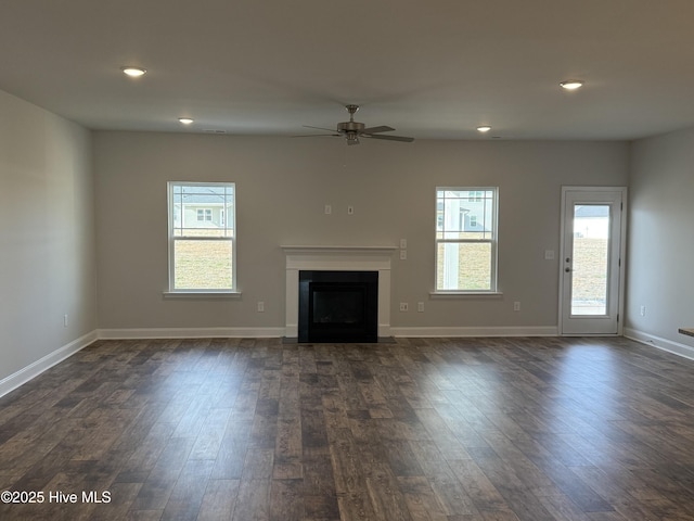 unfurnished living room with plenty of natural light, a fireplace, baseboards, and dark wood-style flooring