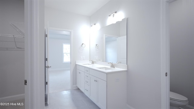 full bathroom with double vanity, a sink, toilet, and baseboards