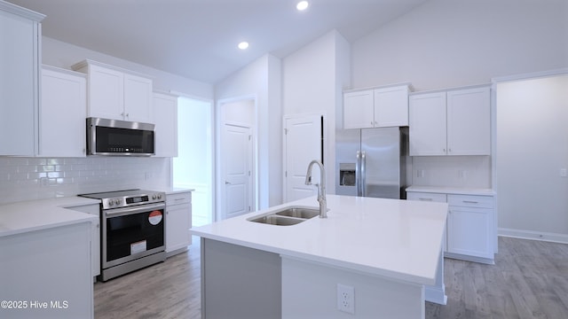 kitchen featuring lofted ceiling, a sink, white cabinets, appliances with stainless steel finishes, and an island with sink