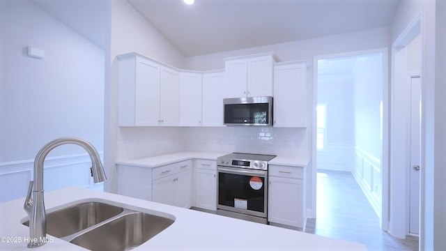 kitchen featuring light countertops, decorative backsplash, appliances with stainless steel finishes, white cabinets, and a sink