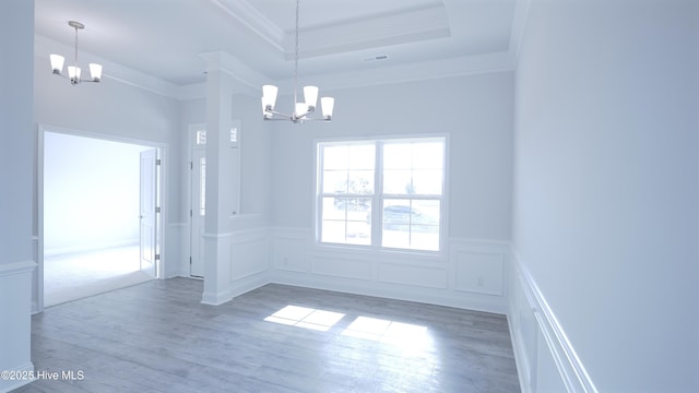 unfurnished room featuring an inviting chandelier, a tray ceiling, light wood-style floors, and crown molding