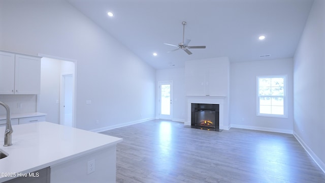 unfurnished living room with baseboards, a fireplace with flush hearth, ceiling fan, light wood-type flooring, and recessed lighting