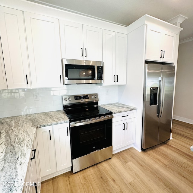 kitchen featuring appliances with stainless steel finishes, tasteful backsplash, white cabinets, light stone counters, and light hardwood / wood-style floors